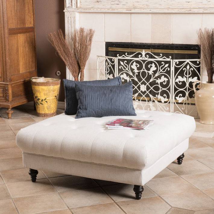 квадратная белая оттоманка с подушками возле камина