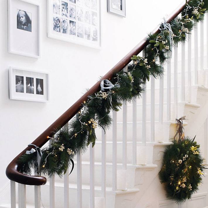 хвоя и гирлянды на перилах лестницы в новогоднем декоре