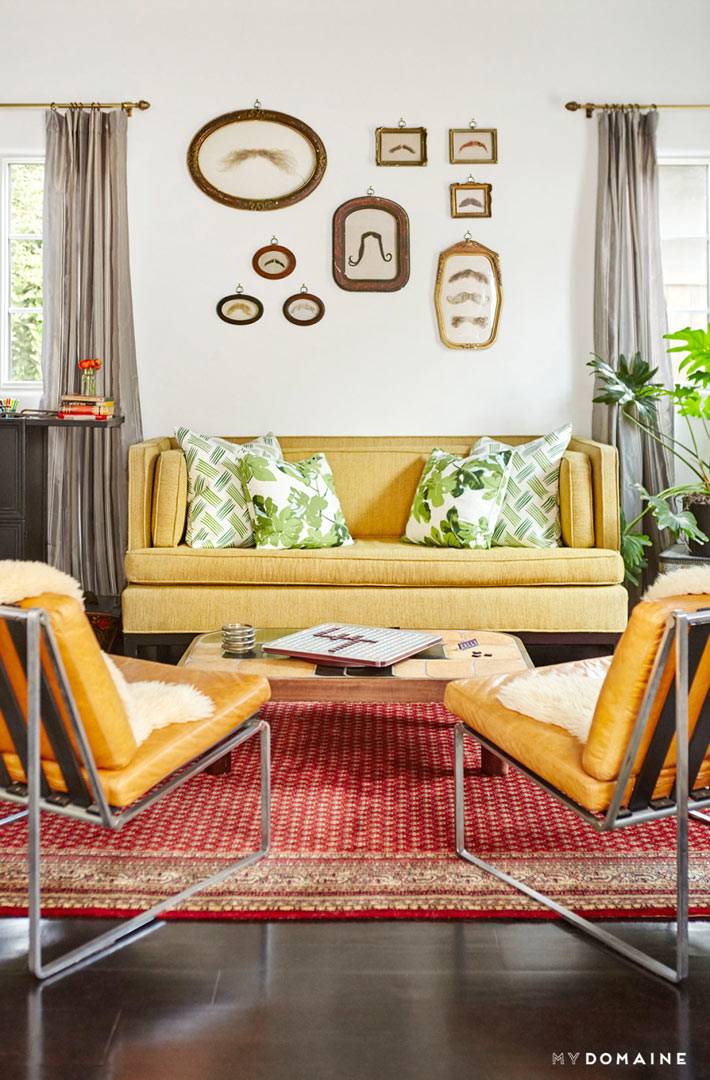 Мягкая мебель желтого цвета и рисунки усов в рамах на стене гостиной